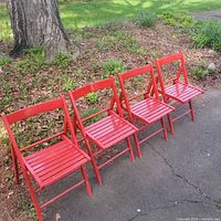 Four red painted wood folding chairs lined up outdoors