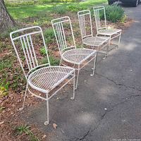 Four white wrought iron chairs lined on driveway