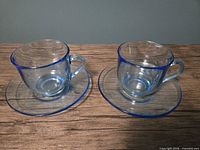 Two light blue glass teacups each on matching saucer