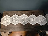 Full view of the white cotton crochet table runner on a dark surface showing pattern and length
