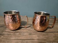 Two hammered copper mugs side by side showing exterior finish, interior lining and handles