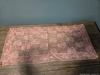 Top view of pink lace floral rectangular table runner on wooden surface