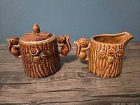 Front view of sugar bowl with lid and creamer showing squirrel handles and maple leaf motifs