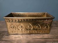 Oblique view of brass planter showing front embossing and patina