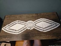 Full view of white cotton crochet table runner on dark surface highlighting overall shape and pattern