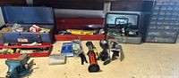 Overview of workbench with three open metal toolboxes, flashlights, reciprocating saw attachment, drill bit packs, and parts organizer
