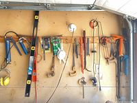 Assortment of hanging hand tools including caulking guns, levels, clamps, earmuffs
