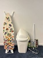 Group shot showing ironing board, trash can with lid, packaged puck lights, shower head set, and tension rod leaning against wall