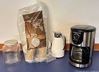Group photo showing glass storage jar, sealed Café Express cups pack, white thermal jug, KitchenAid coffee maker