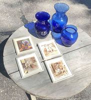 Three cobalt blue glass vases and four framed ceramic tiles displayed on round wooden table