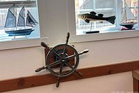 Ship wheel mounted on wall below window with model boat and fish sculpture visible