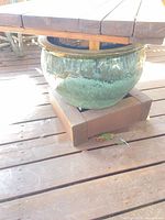 Side view showing wood table top, base, and green glazed planter seated within
