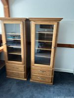 Front view of both light oak display cabinets showing glass doors, shelves, and drawers