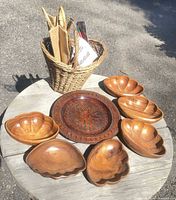 Overview of six carved wood bowls, carved platter, wicker basket with contents