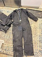 Front view of Super Tuff coverall laid flat showing quilted lining, brass snaps, zipper