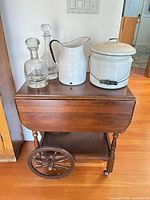 Overall view of wood cart with glass decanters, enamel pitcher and pot on top