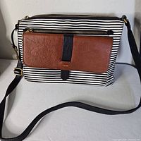 Front view showing striped body, brown leather pocket, zip-top, strap