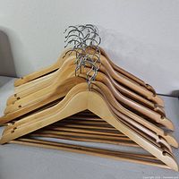 Stacked view of 18 wooden hangers showing wood grain and chrome hooks