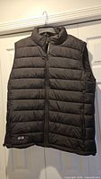 Full front view of black Kodoku heated vest hanging on hanger