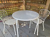 Full view of white metal round table with two chairs