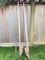 Pair of wooden stilts and tennis racket leaning against fence