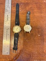 Two wristwatches beside 12-inch ruler showing size and strap condition