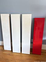 Front view of four IKEA Lack shelves—three white, one red—standing upright showing size and color
