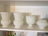 Four milk glass vases lined on shelf