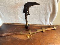 Sword with scabbard and sickle machete on tabletop