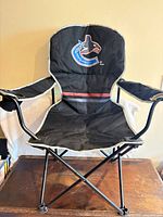 Front view of black folding camping chair showing logo, cup holder, frame and fabric condition