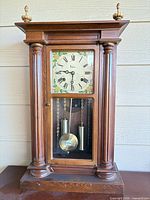 Full view of mantel clock showing wood case, columns, glass door, finials