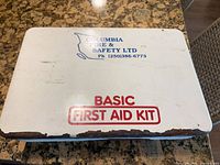 Closed metal first aid kit case showing Columbia Fire & Safety Ltd branding and rusted edge