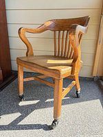 Full view of wooden bankers chair with armrests and casters