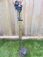 Full view of Yardworks gas string trimmer leaning against fence