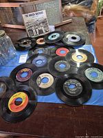 Group shot of approximately 15 7-inch vinyl singles on assorted labels, one in picture sleeve