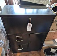 Front view of black metal filing cabinet showing key, two drawers, cabinet door