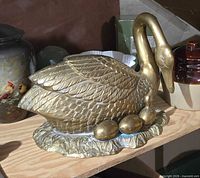 Front angled view of brass swan sculpture with eggs on base