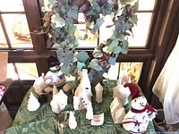Overall view of ceramic village pieces, plush snowmen, metal angel and fabric on table