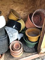 Assorted terracotta, ceramic, metal and plastic planters stacked inside shed