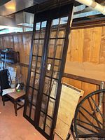 Pair of dark brown French doors leaning against wall showing full height and glass pane grid