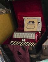 Accordion in open hard case with sheet music and torn cloth cover