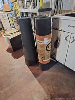 Two upright rolls of black roofing felt beside sink; labeled wrapper visible on one