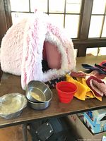 Pink faux fur cave bed, stainless bowls, red silicone bowl, clothing pile