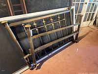 Headboard and footboard leaning against wall showing brass finials and iron frame