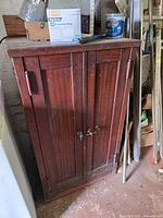 Front view of closed faux-wood metal cabinet showing double doors and brass loop handles