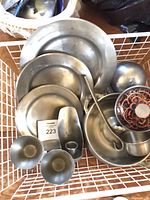 Assorted pewter plates, goblets, scoop, ladle, covered dish and bowls gathered in basket