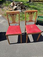 Front view of both wooden chairs showing red vinyl seats and decorative backrests