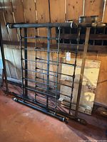 Wrought iron headboard and footboard leaned against wall showing brass accents and overall condition