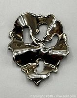 Front view of abstract silver-tone brooch showing crumpled form and openings