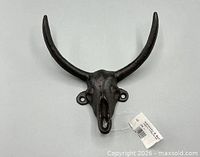 Front view of cast iron bull skull hook showing horns, hook, mounting holes, attached tag